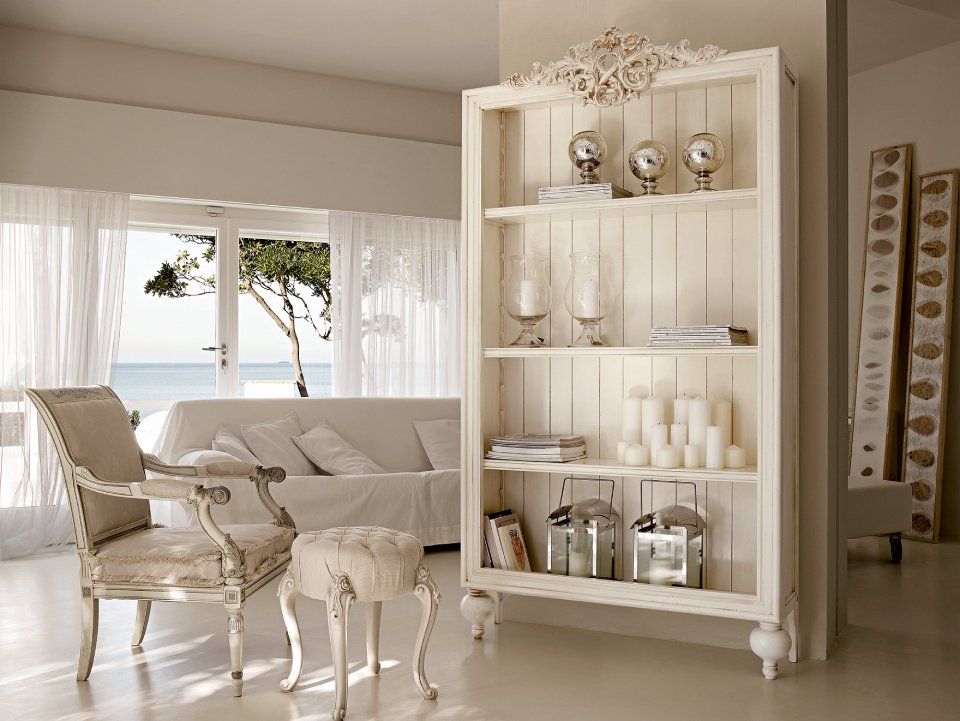 Libreria bianca con oggetti decorativi; sedia e pouf in una stanza bianca con vista sull'oceano.