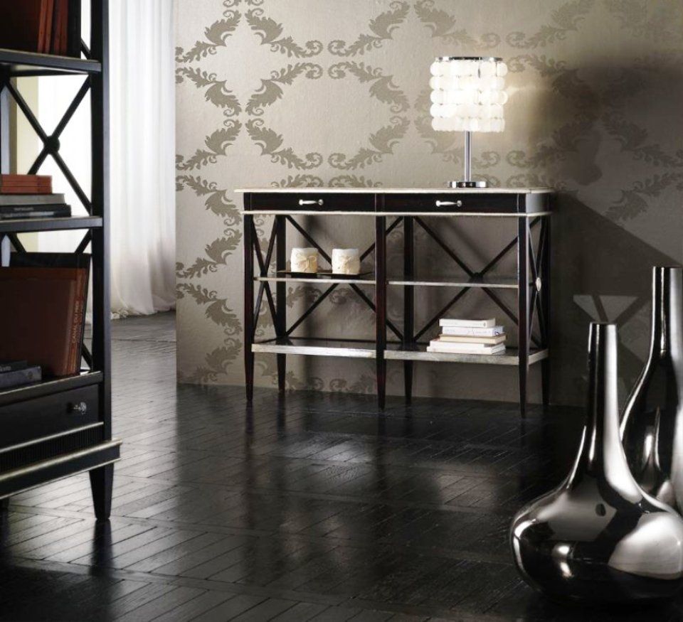 Elegante consolle con vasi argentati, libri e lampada, contro una parete decorata, su pavimenti in legno scuro.