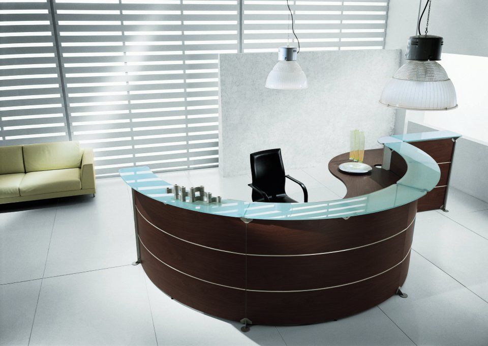 Moderna reception da ufficio con piano in legno marrone e vetro, sedia nera e divano color crema.