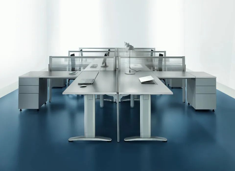 Moderni cubicoli per ufficio con scrivanie grigie e pavimento color verde acqua.