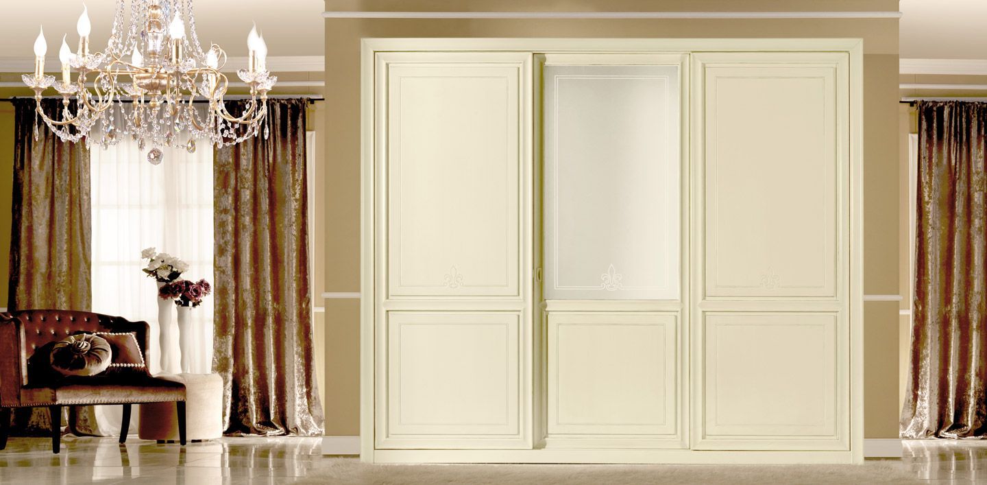 Armadio color crema con porta scorrevole, situato in una lussuosa stanza con lampadario decorato e tende.