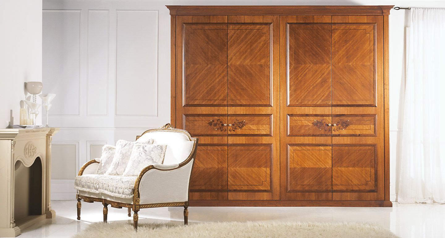 Armadio in legno con ante intarsiate e sedia decorativa in una stanza luminosa.
