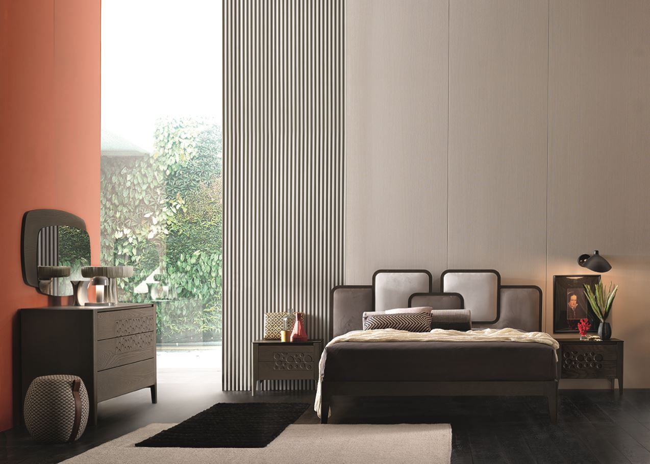 Camera da letto con mobili moderni: letto scuro, cassettiera, comodini. Pareti neutre, accenti arancioni, ampia finestra.