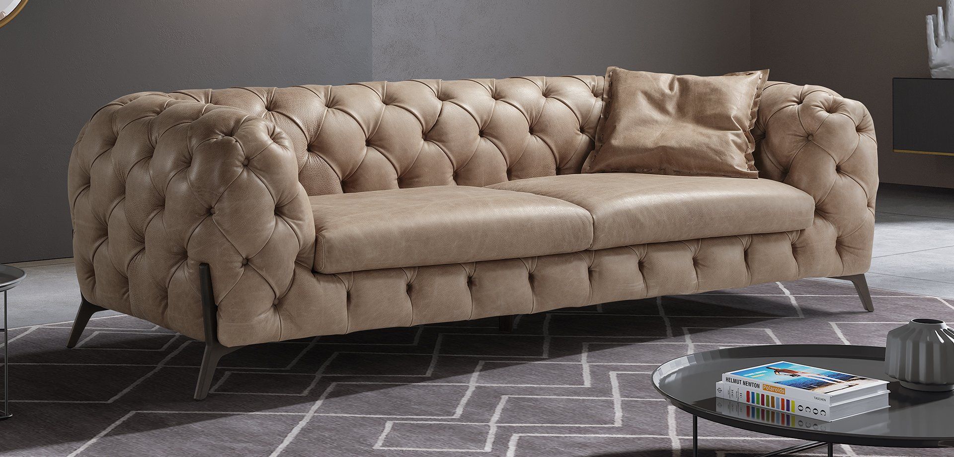 Divano Chesterfield capitonné color marrone con cuscino, su un tappeto fantasia.