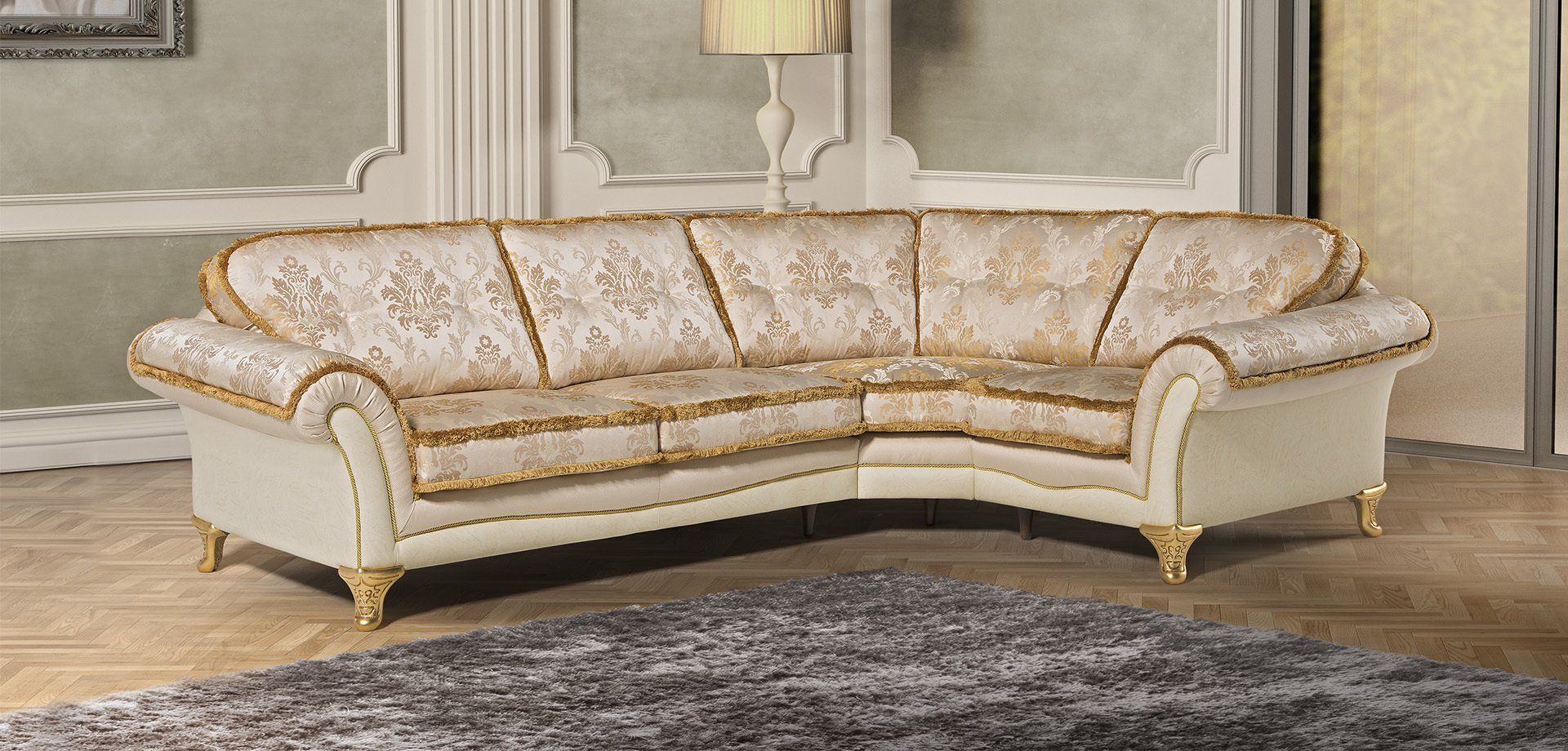 Divano componibile color crema con rifiniture dorate decorate, appoggiato a una parete con modanature decorative.