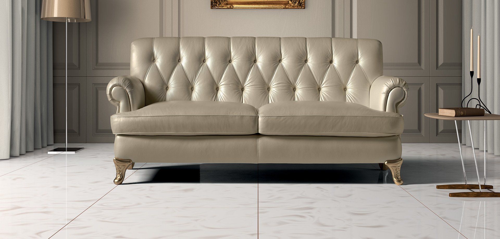 Divano capitonné color crema in una stanza con pavimento in marmo bianco, una lampada da terra e un tavolino laterale.