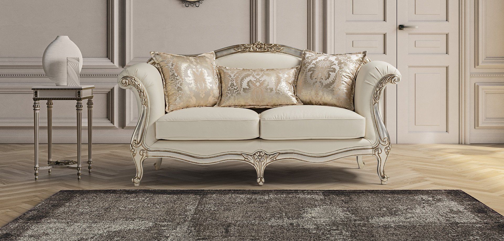 Un divano color crema con rifiniture decorative e cuscini è appoggiato su un tappeto davanti a una parete.