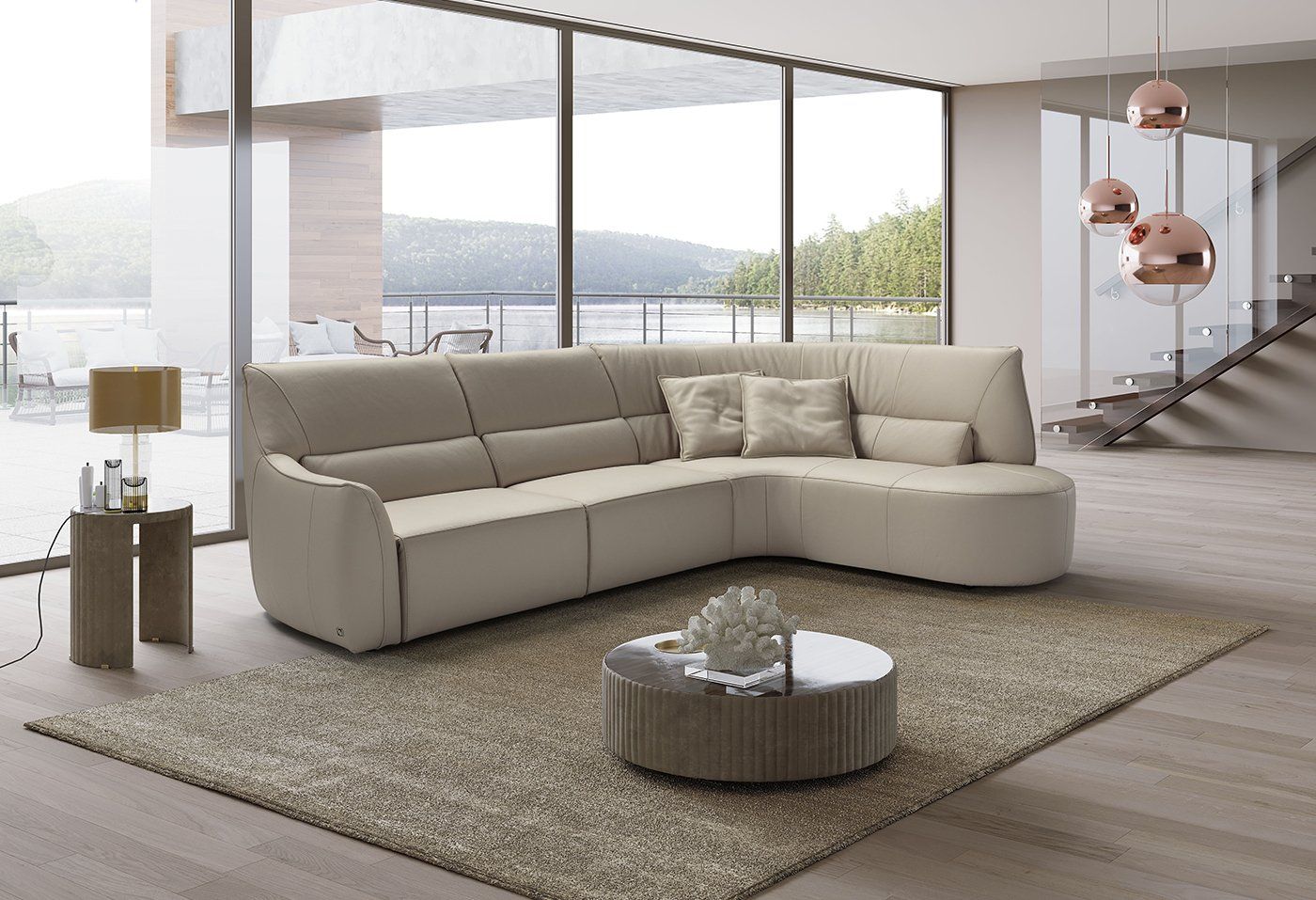 Divano componibile beige in un soggiorno moderno con ampie finestre che si affacciano sull'acqua e un tappeto.