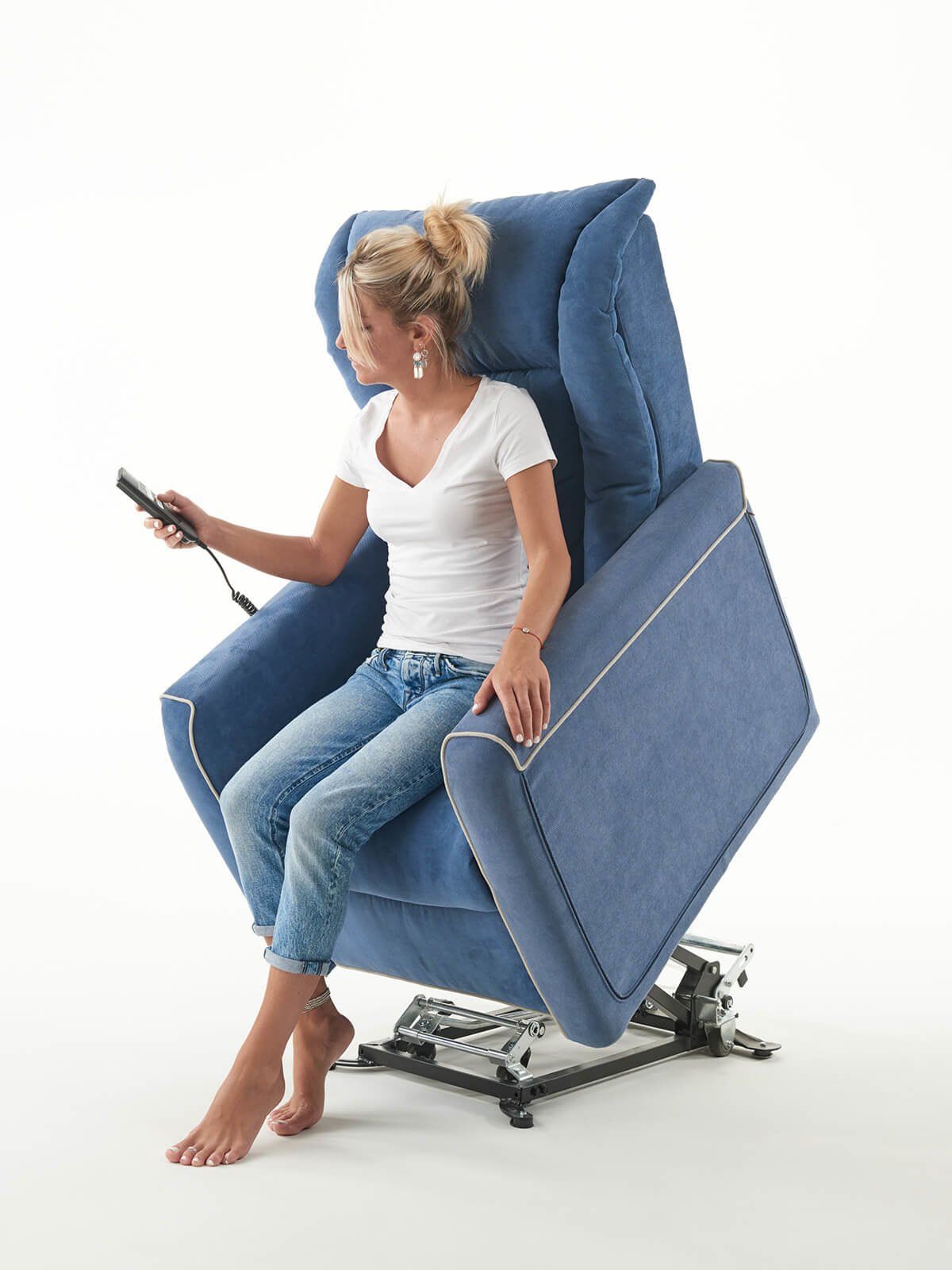 Donna su poltrona elevatrice blu che usa un telecomando. Sfondo bianco.
