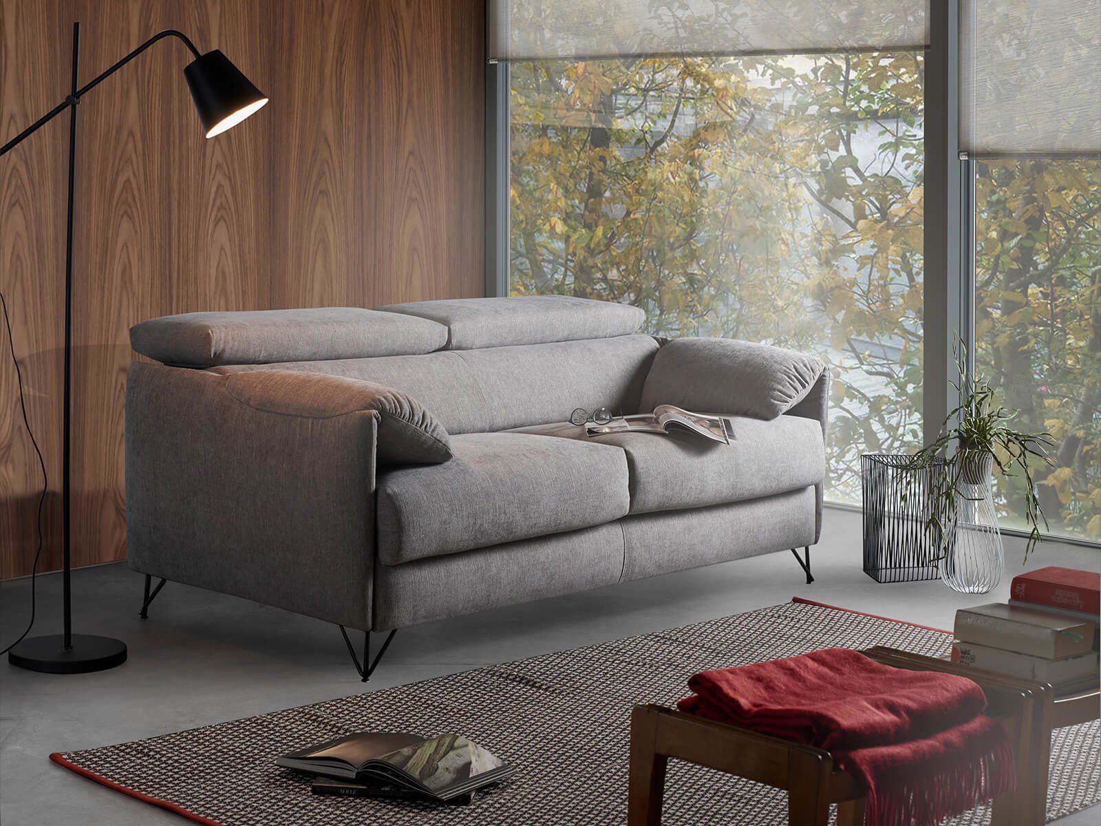 Divano grigio in un soggiorno moderno con lampada da terra, tappeto e vista dalla finestra.
