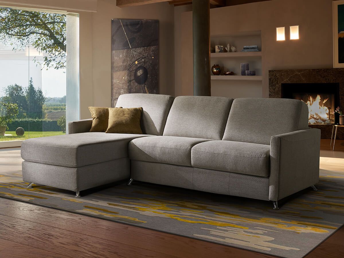 Divano componibile grigio con chaise longue in un soggiorno; camino, finestra, opere d'arte.