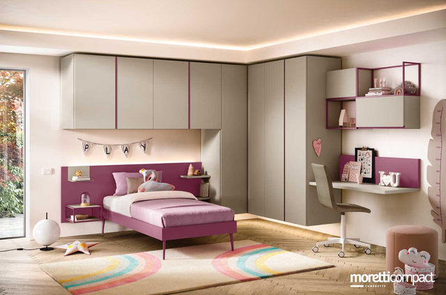 Cameretta per bambini viola e grigia con letto, scrivania, armadietti e tappeto arcobaleno.