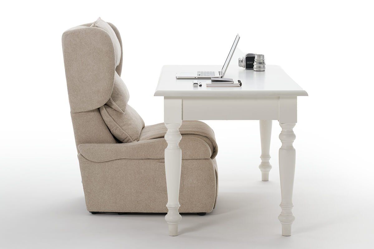 Poltrona color crema e scrivania bianca con computer portatile, cuffie e oggetti su sfondo bianco.