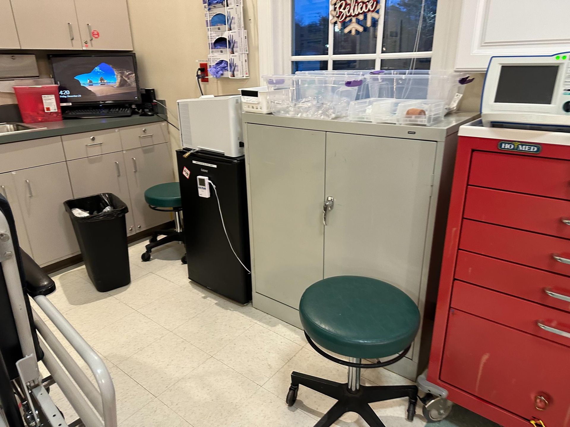 A hospital room with a green stool and a red cart