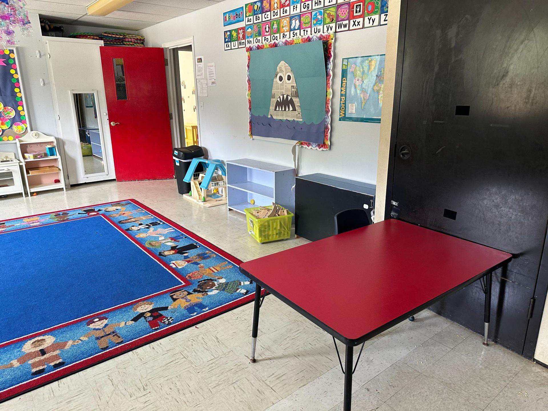 A classroom with a red table and a blue rug.
