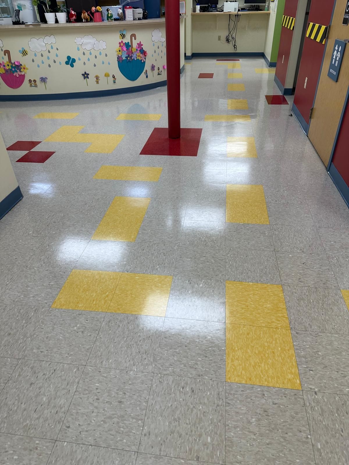 A hallway with yellow and white tiles and a red pole in the middle.