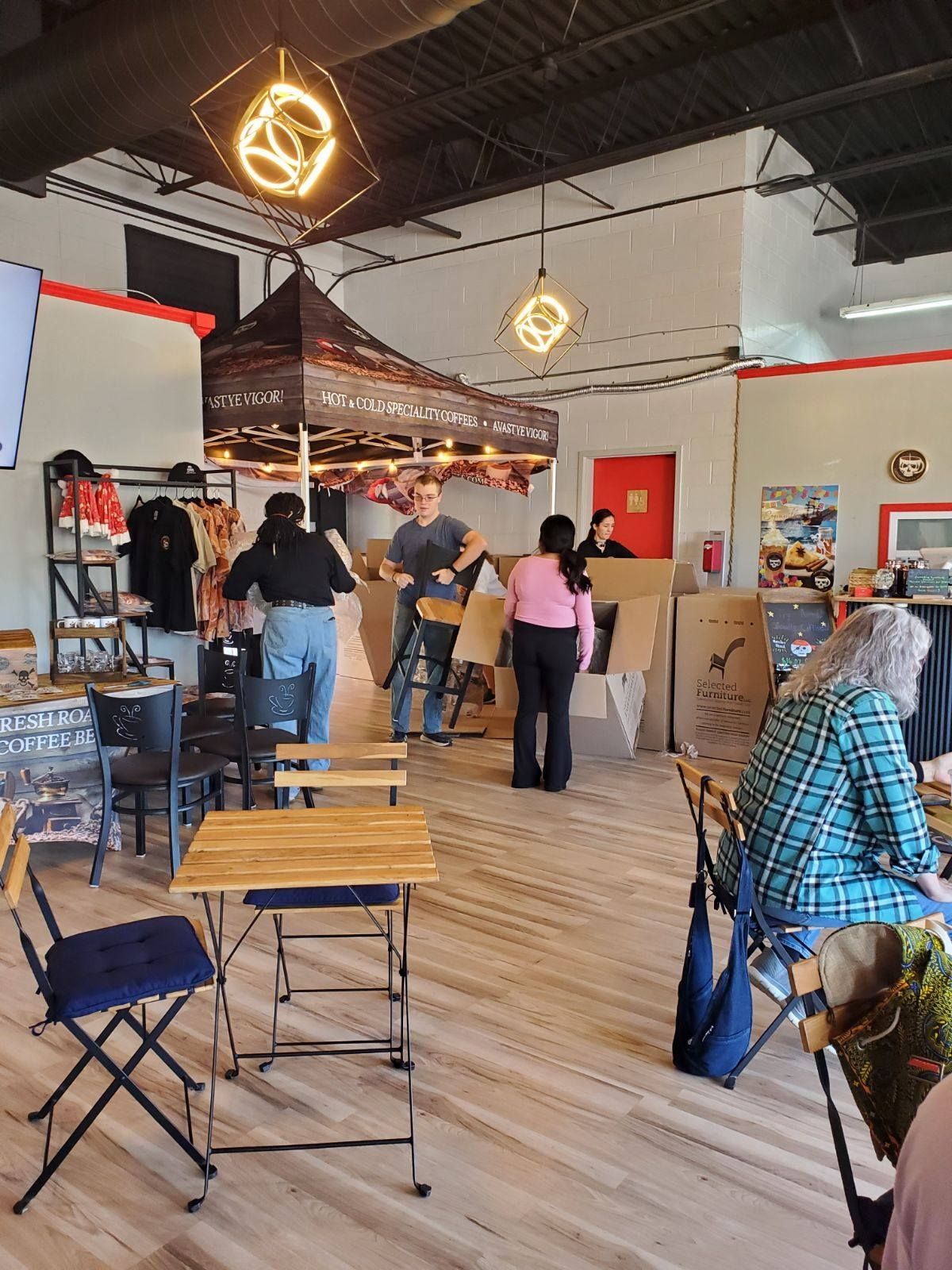 People set up a booth and work in a bright, open space with wooden floors, folding chairs, and industrial lighting.