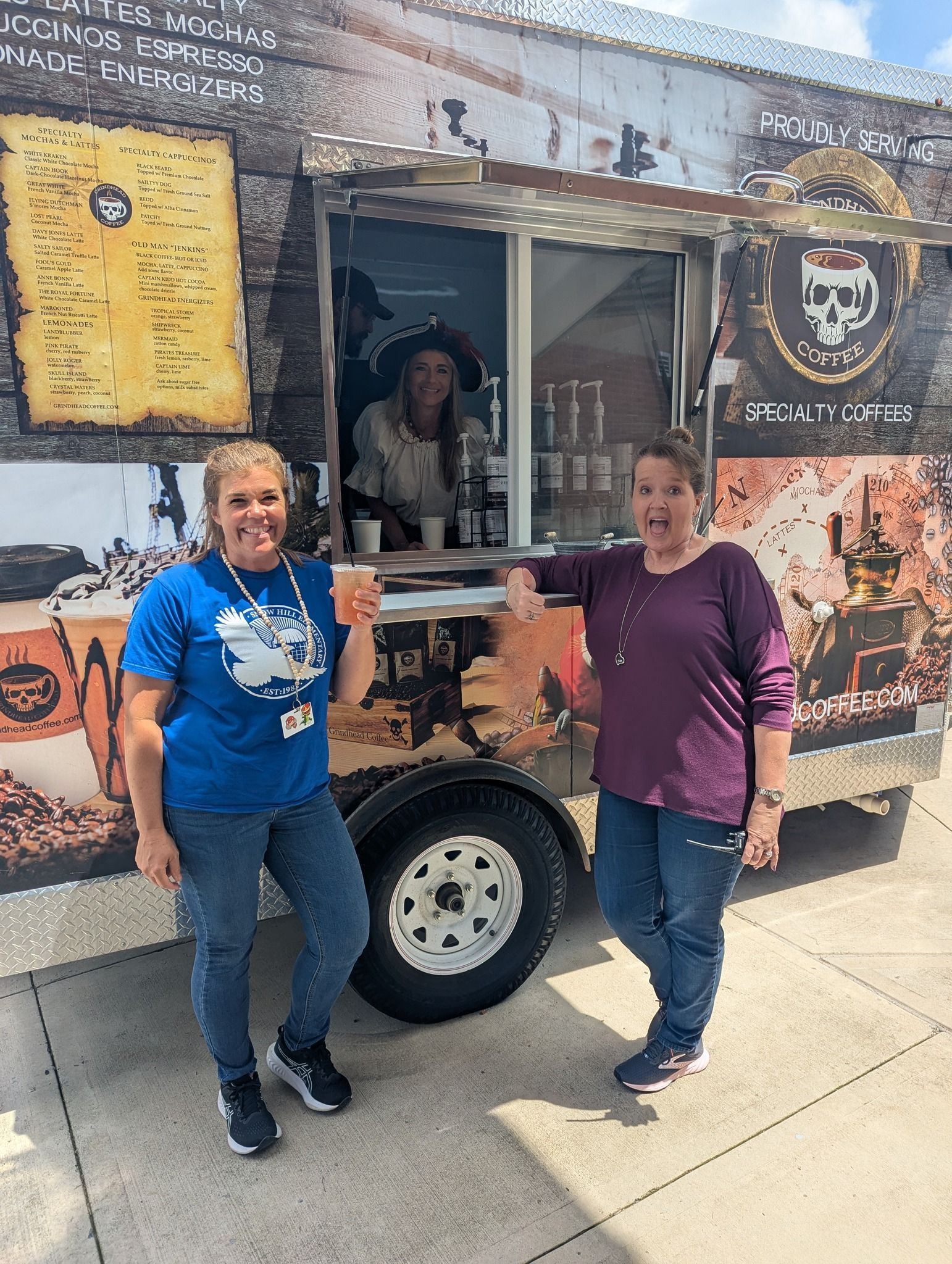Two people stand smiling in front of a coffee food truck, with a third person visible inside the service window.