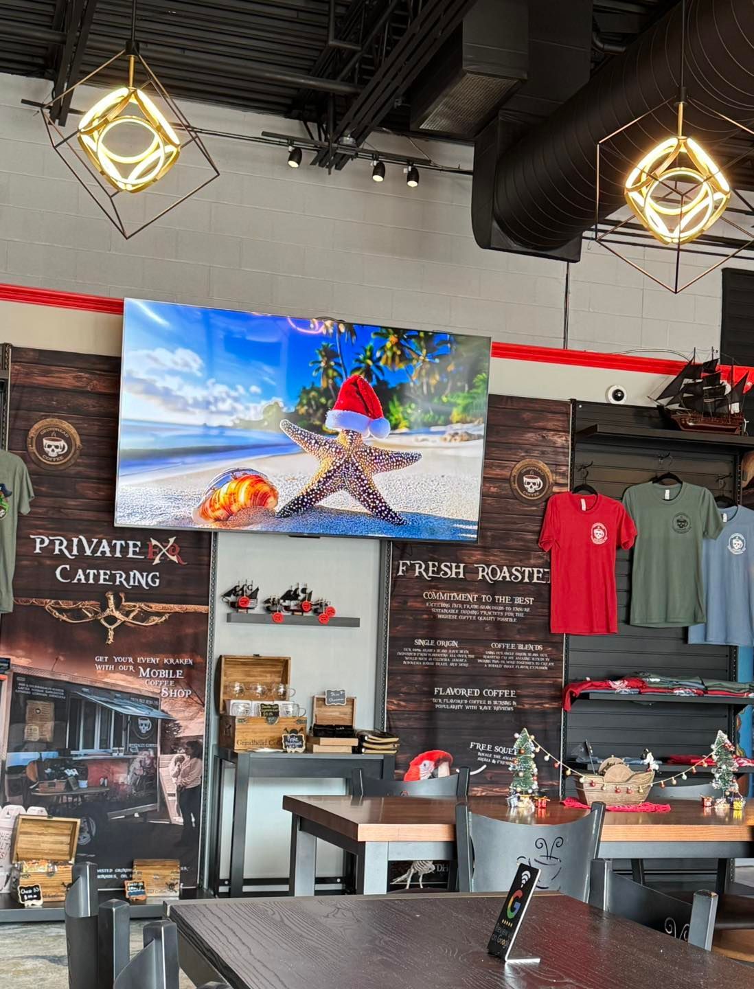 A cafe interior with a television displaying a starfish in a Santa hat, merchandise, signage, and tables.