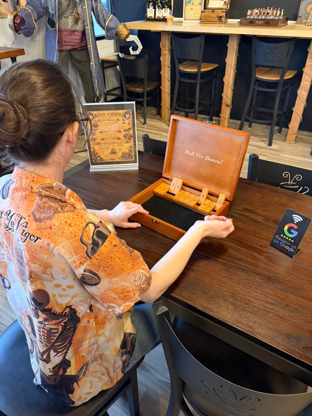 A person in a patterned shirt sits at a dark wood table interacting with an open, decorative box inside a shop.