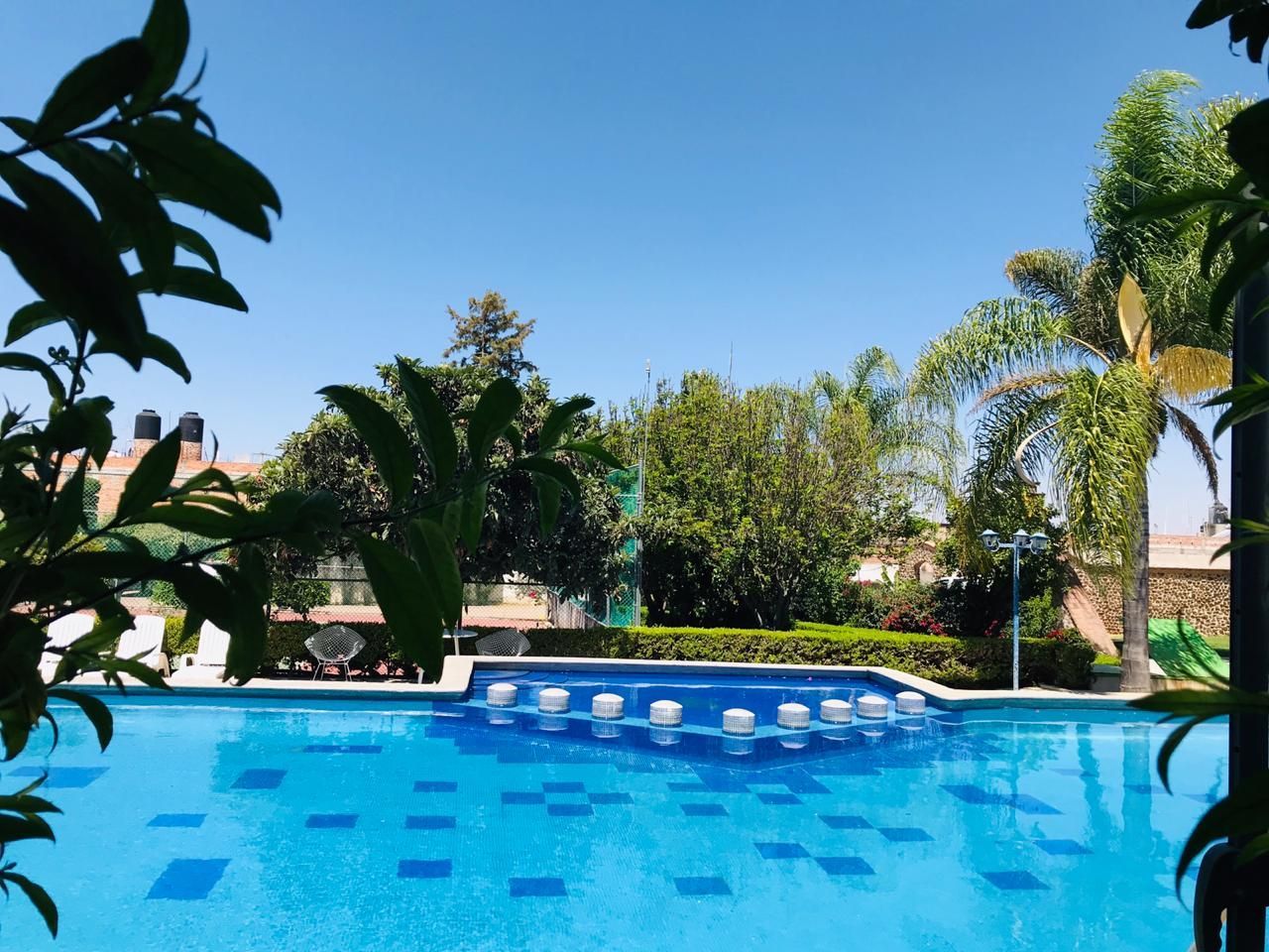 Piscina al aire libre en un edificio blanco con gente nadando y tomando el sol en un día soleado.