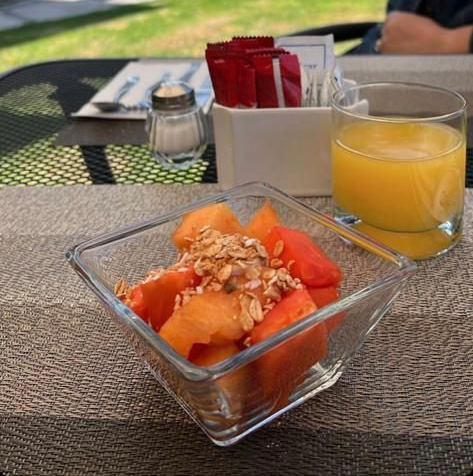 Mano sosteniendo un tazón de ensalada de frutas con fresas, plátano y bayas sobre una superficie blanca.