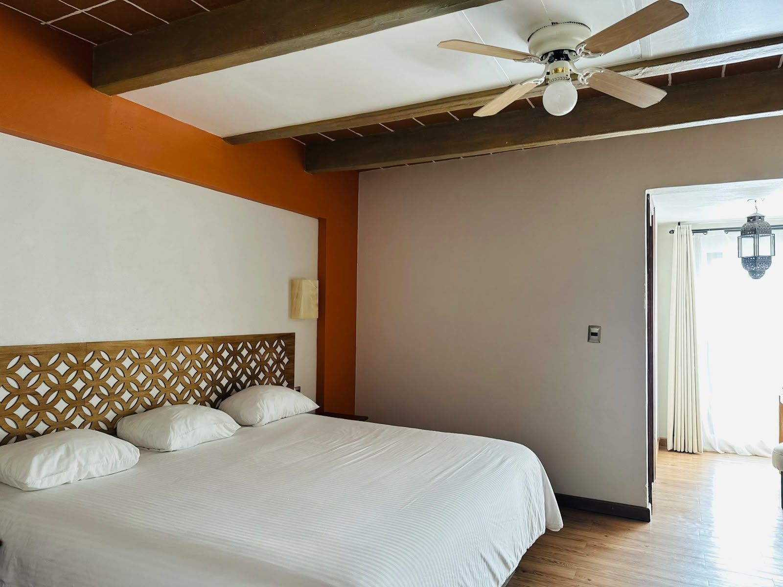 Dormitorio con cama de madera tallada, vigas a la vista, puerta arqueada y arte en la pared.