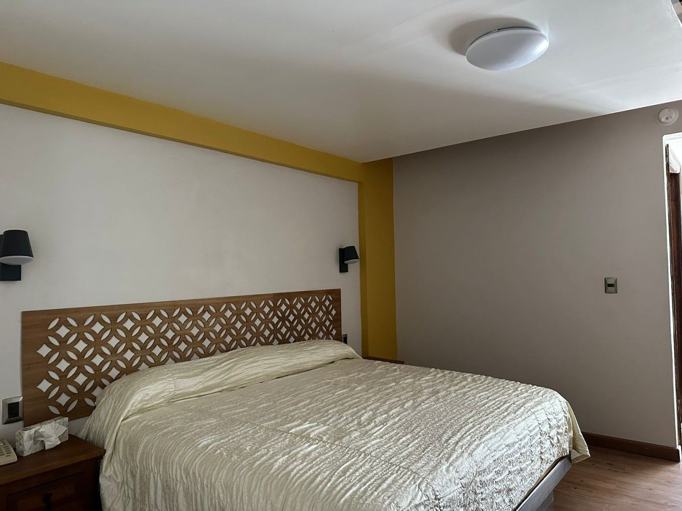 Dormitorio con cama, cabecero estampado, apliques de pared y detalles decorativos en color amarillo.