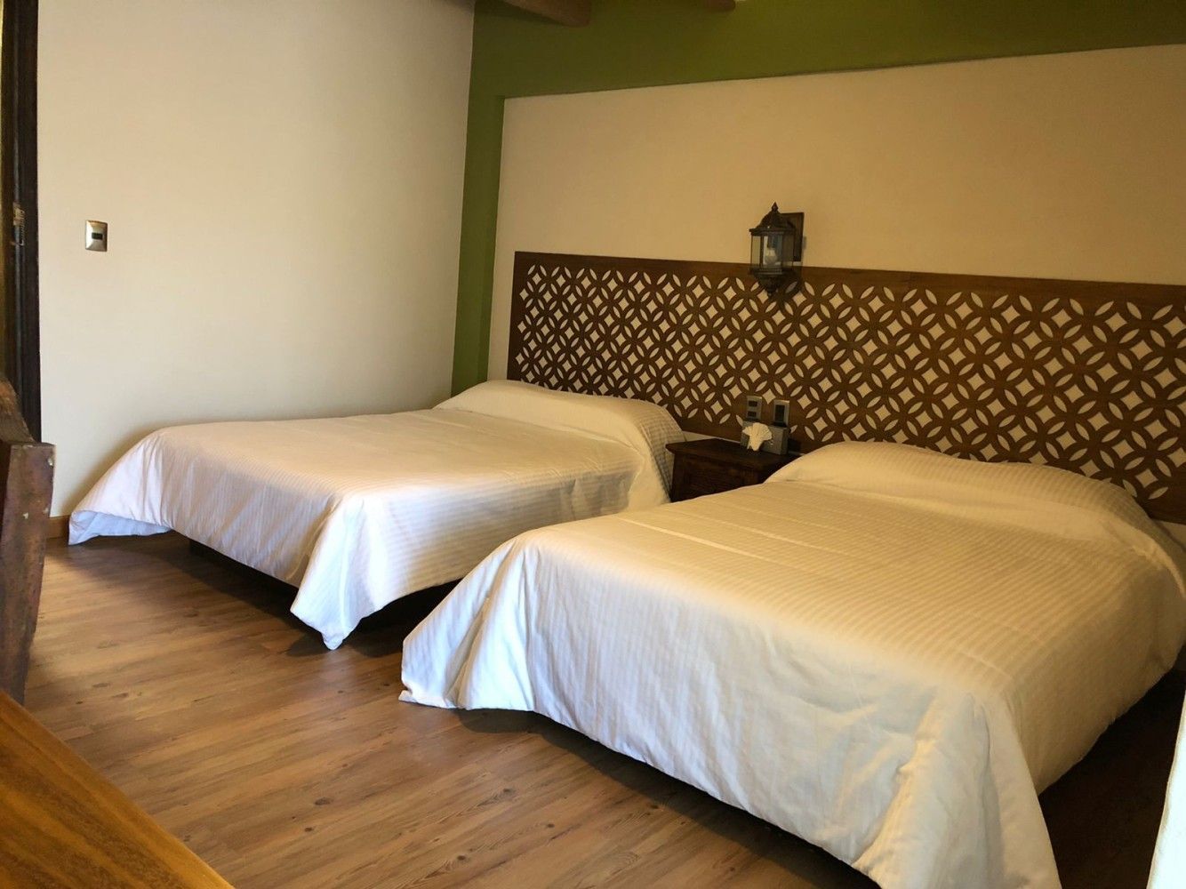 Habitación de hotel con dos camas, sábanas blancas, suelo de madera y cabecero de cama estampado.