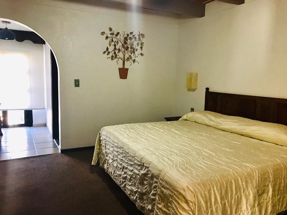 Habitación sencilla con cama, decoración en la pared y una puerta arqueada que da a un pasillo luminoso.