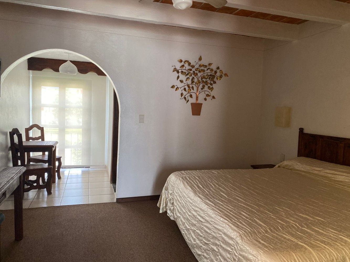 Dormitorio con cama y decoración de pared, con acceso a un comedor con puertas que dan a ventanas luminosas.