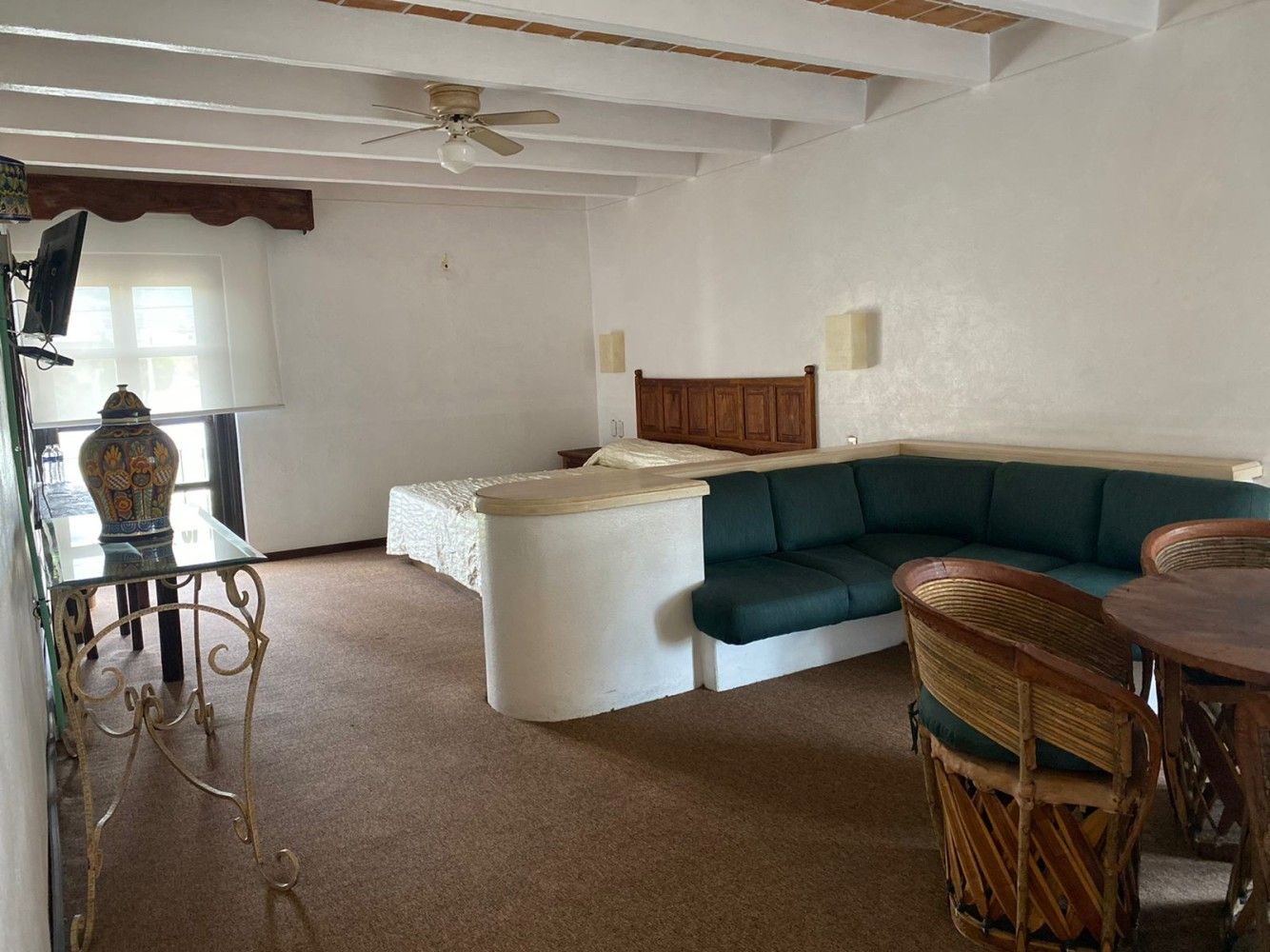 Sala de estar con sofá seccional color turquesa, mesa de mimbre, paredes blancas y una persona junto a la ventana.