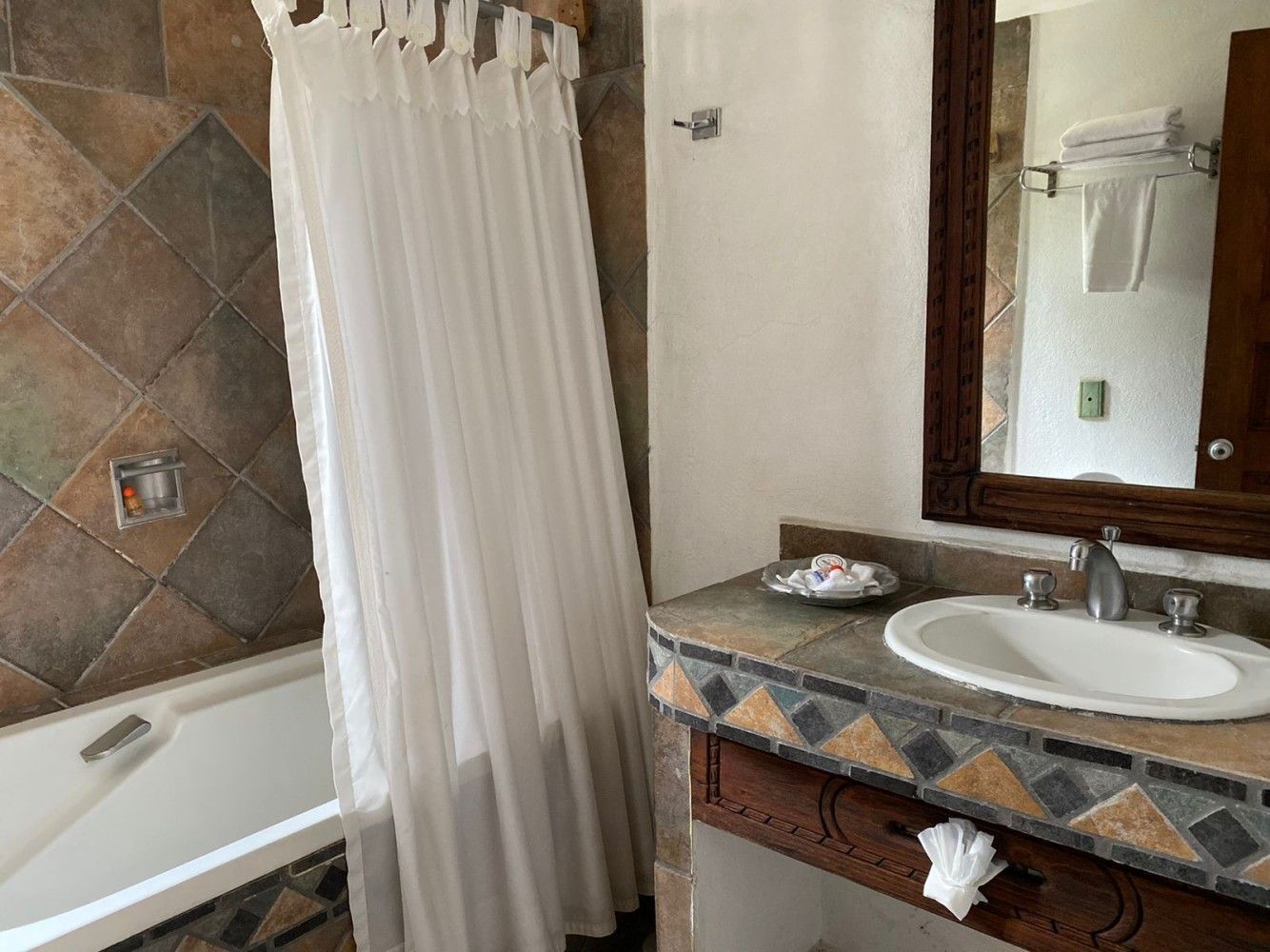 Tocador de baño y bañera con paredes alicatadas, cortina de ducha blanca y espejo de pared.