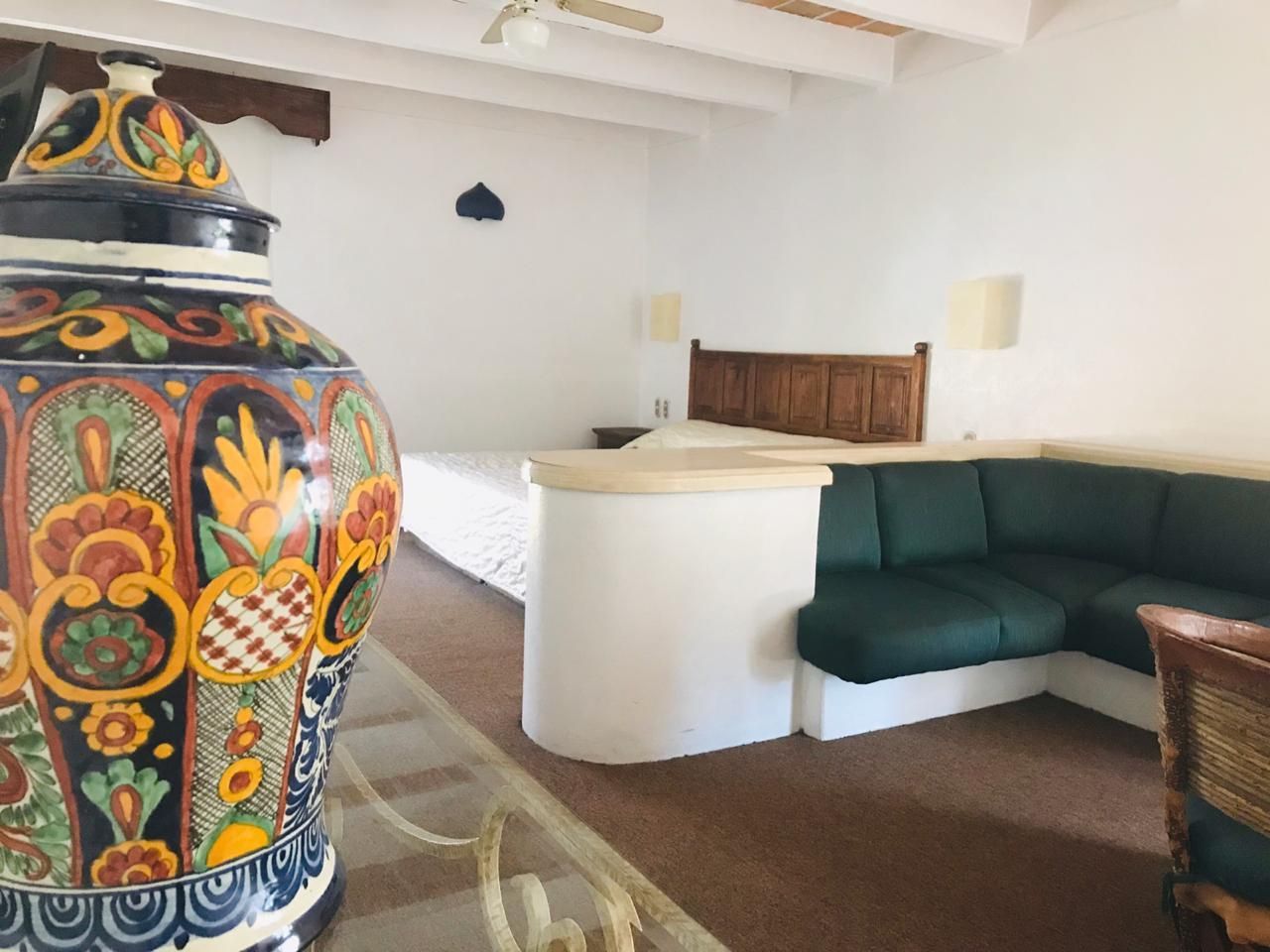 Jarrón de cerámica pintado de colores en una habitación luminosa con sofá seccional color turquesa y estructura de cama de madera.