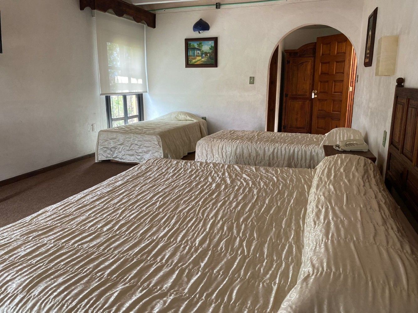 Habitación con tres camas bien hechas, paredes blancas, una puerta de madera y una pequeña ventana.