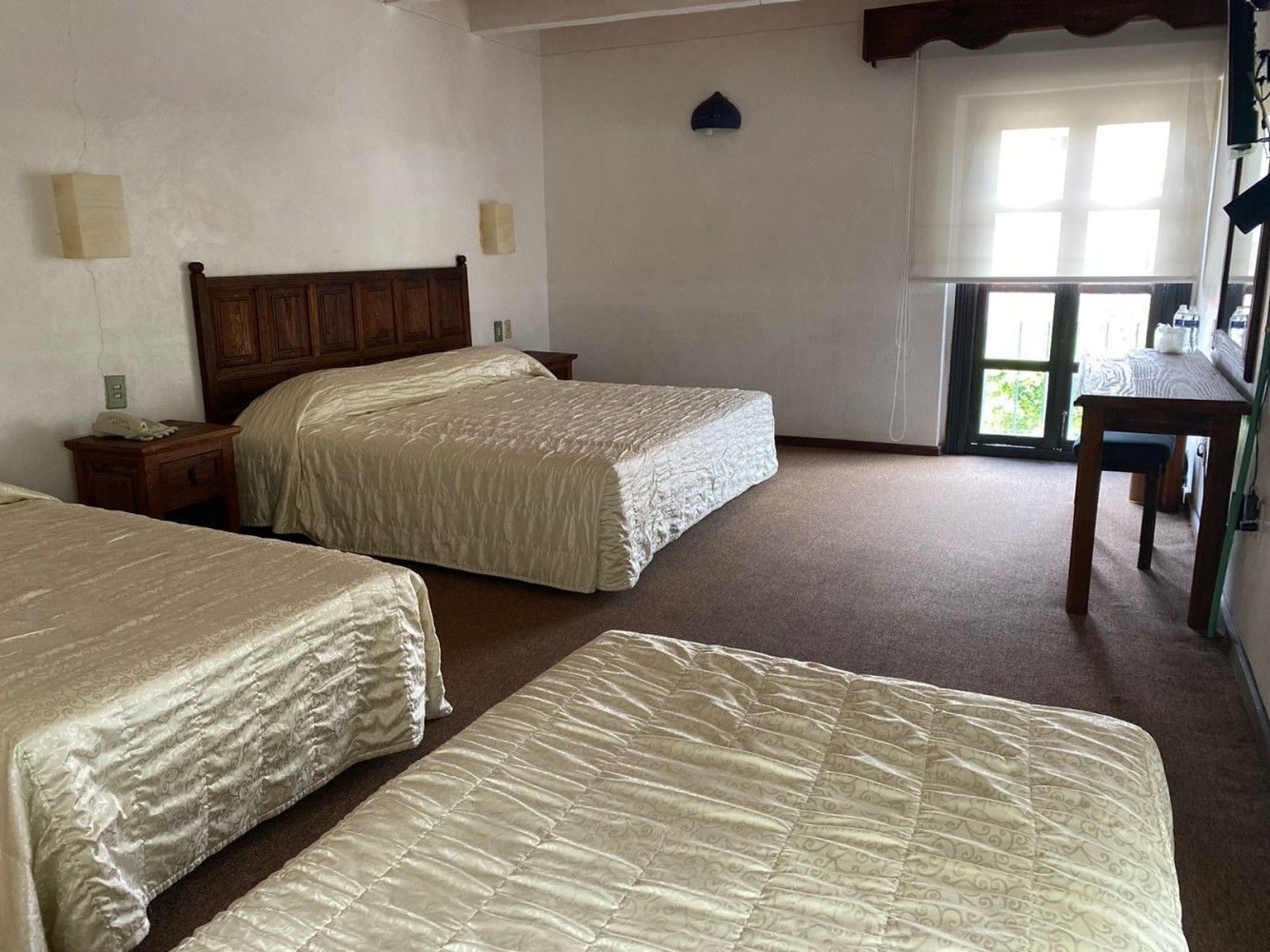 Habitación de hotel espaciosa con tres camas, paredes blancas y una zona de estar junto a la ventana.