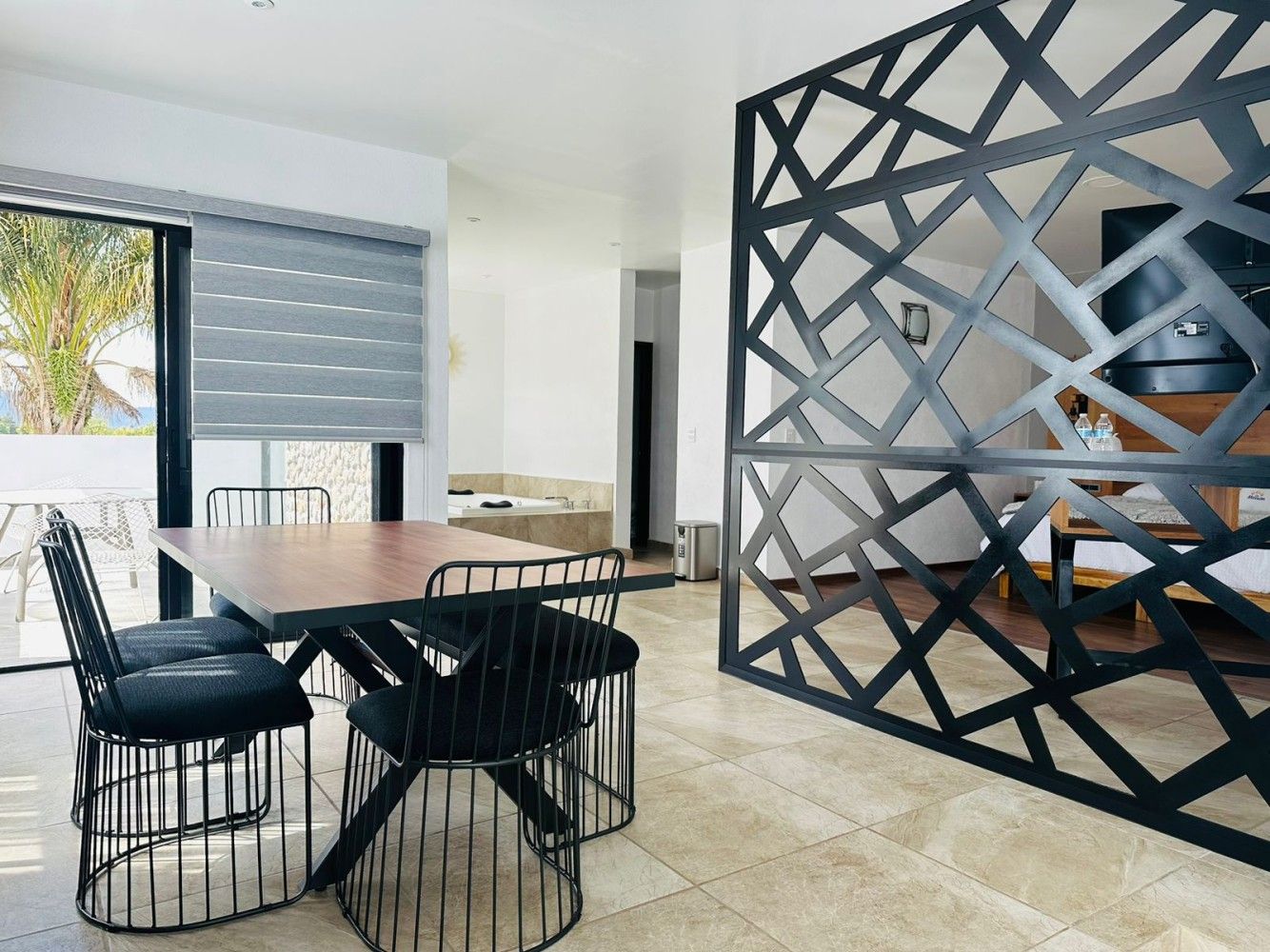 Comedor moderno con sillas negras, mesa de madera, ventana grande y separador de ambientes geométrico.