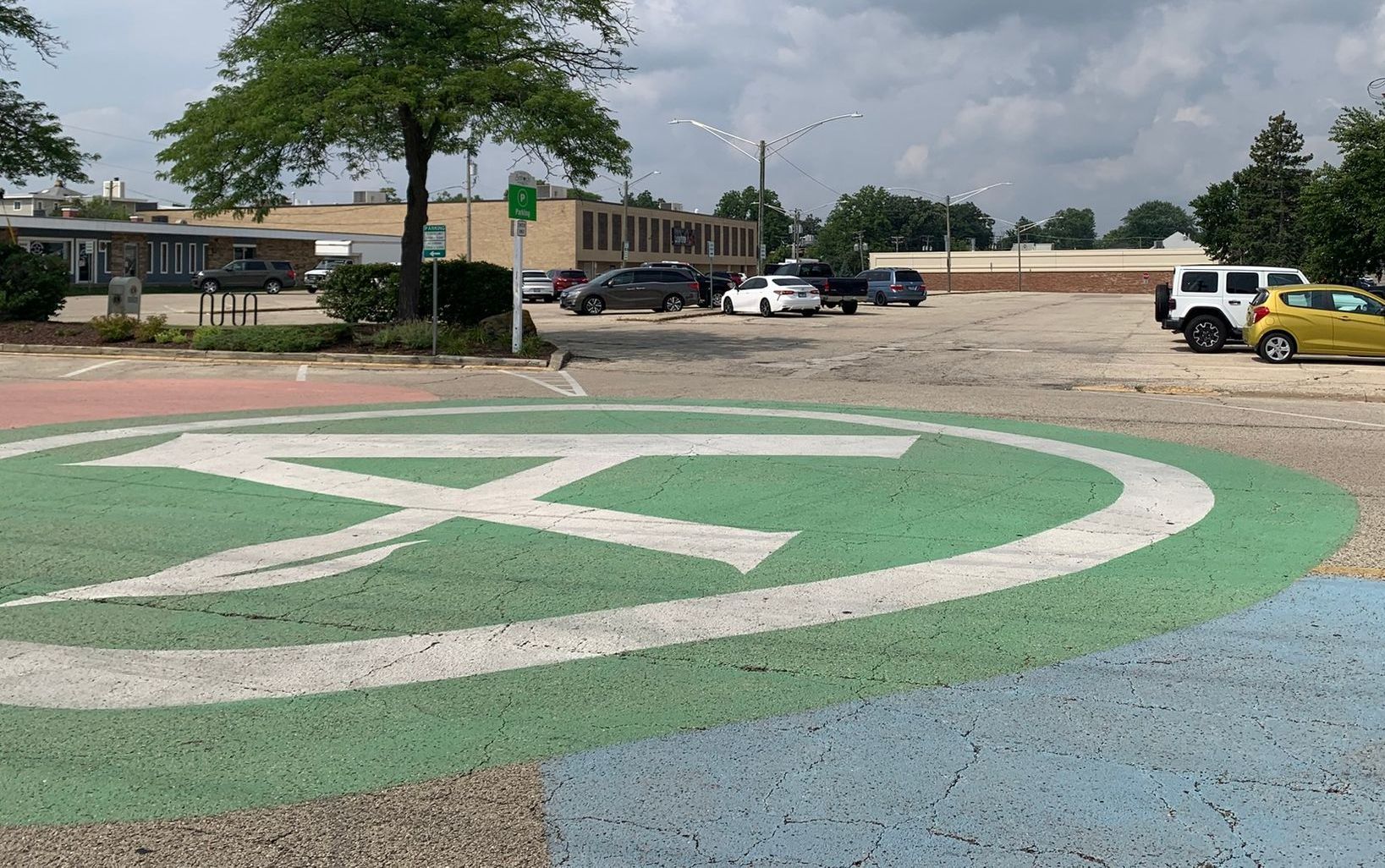 Painted ground art with cars in a parking lot, with a building and tree in the background.