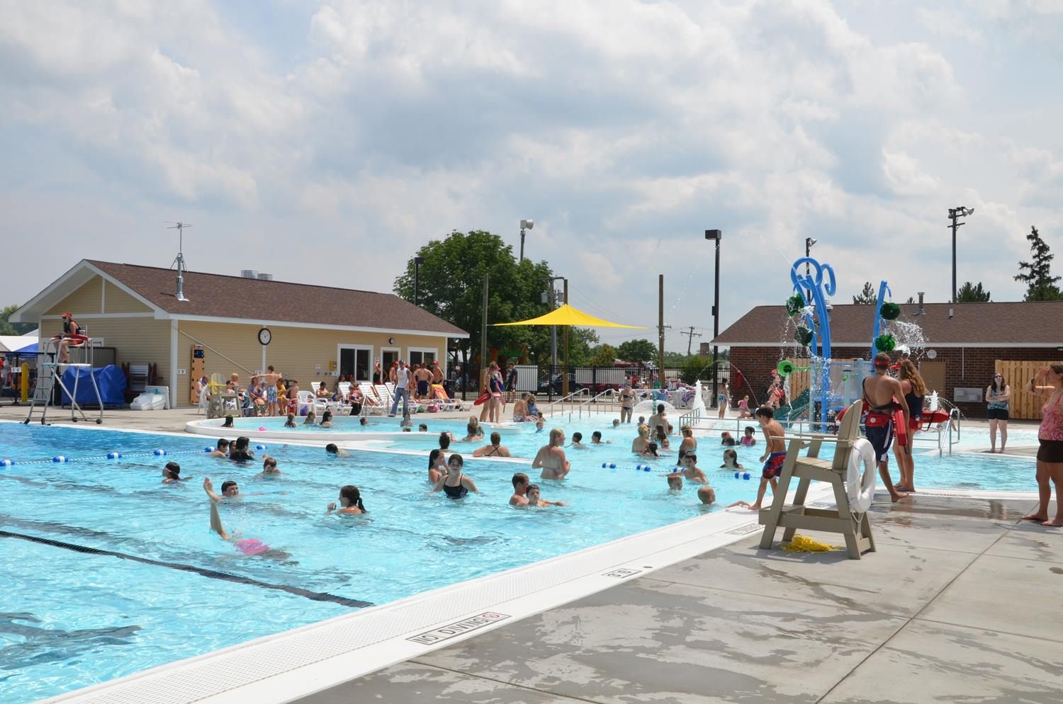 Crowded outdoor swimming pool with people swimming and sunbathing on a sunny day