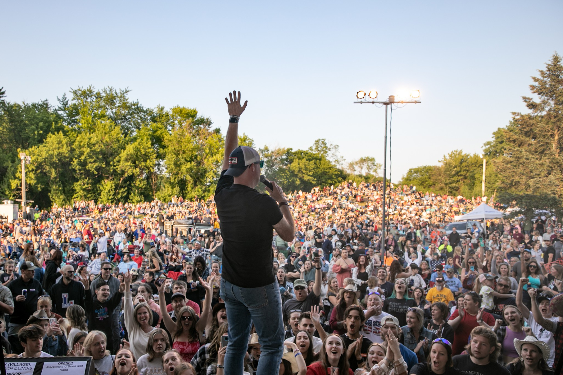 Man on stage with arm raised addressing a large, cheering outdoor crowd.