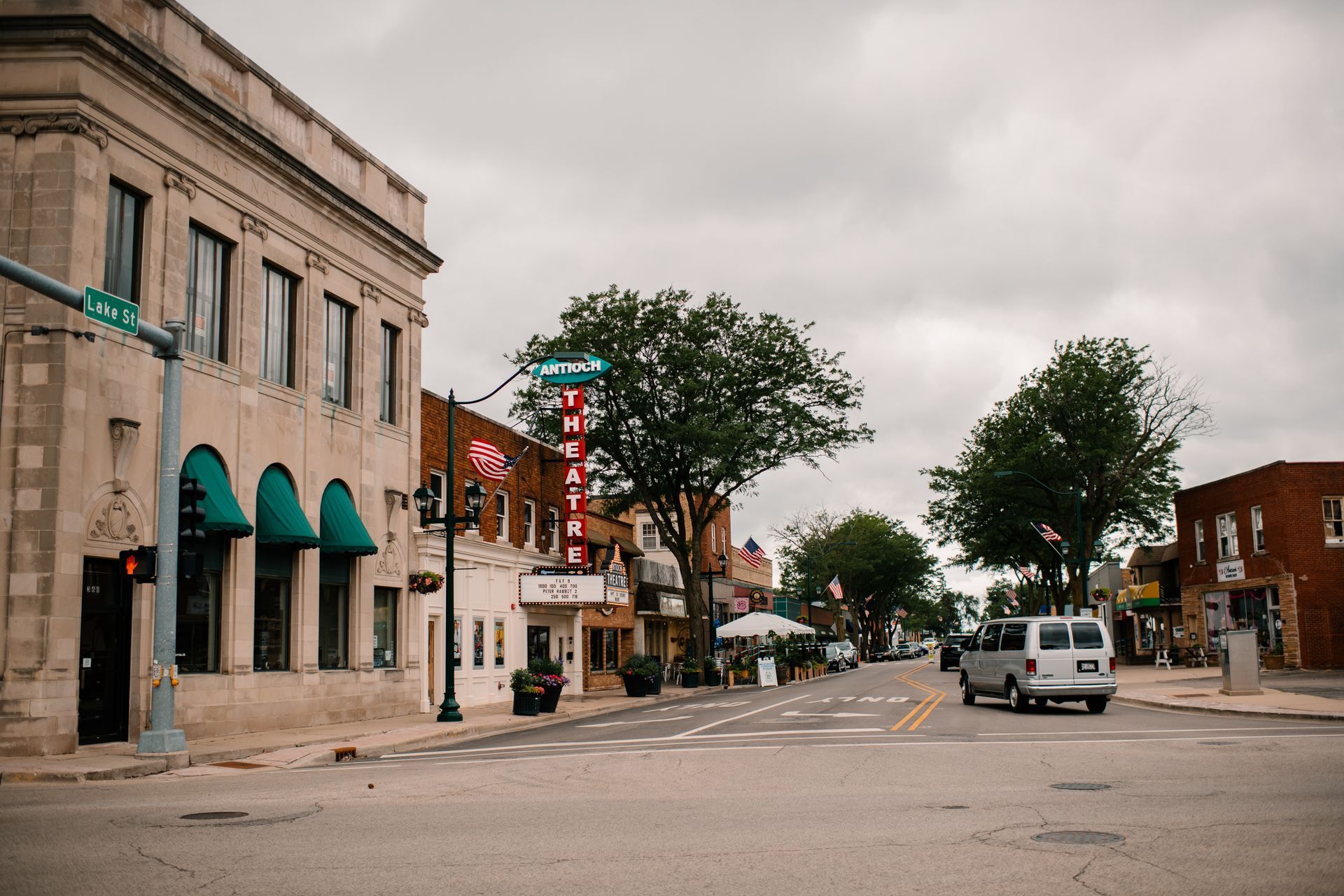 Street scene with buildings, trees, and a vehicle under an overcast sky. A theater sign is visible.
