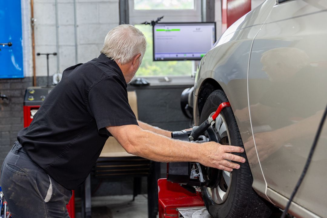 Mechanic aligning a car tire in a garage; computer screen visible.