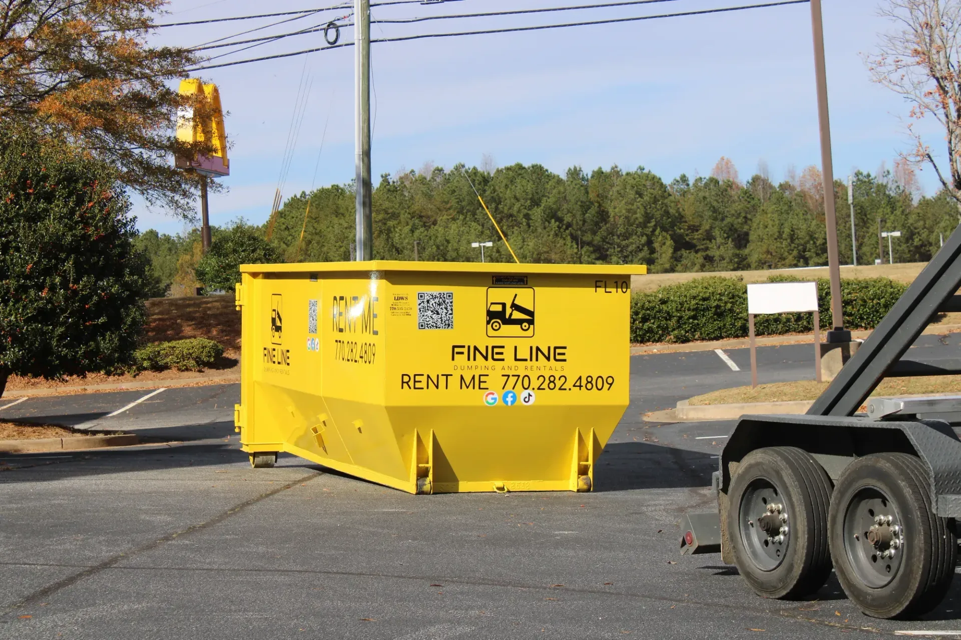 Yellow dumpster labeled “Fine Line” in a parking lot beside a trailer.