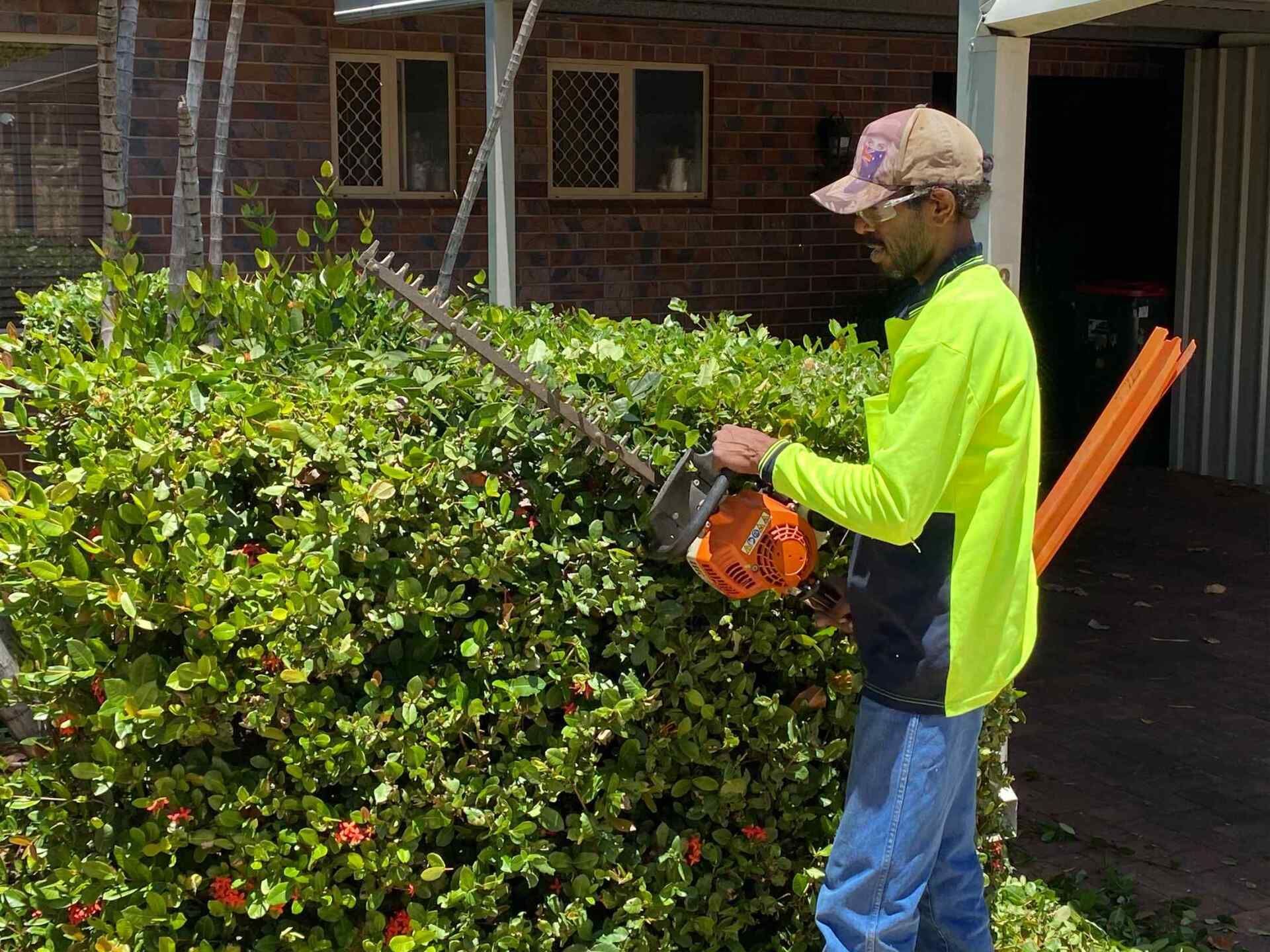 Person in Safety Vest Trimming a Hedge with An Orange Hedge Trimmer — Darrell's Mowing Services in Cloncurry, QLD
