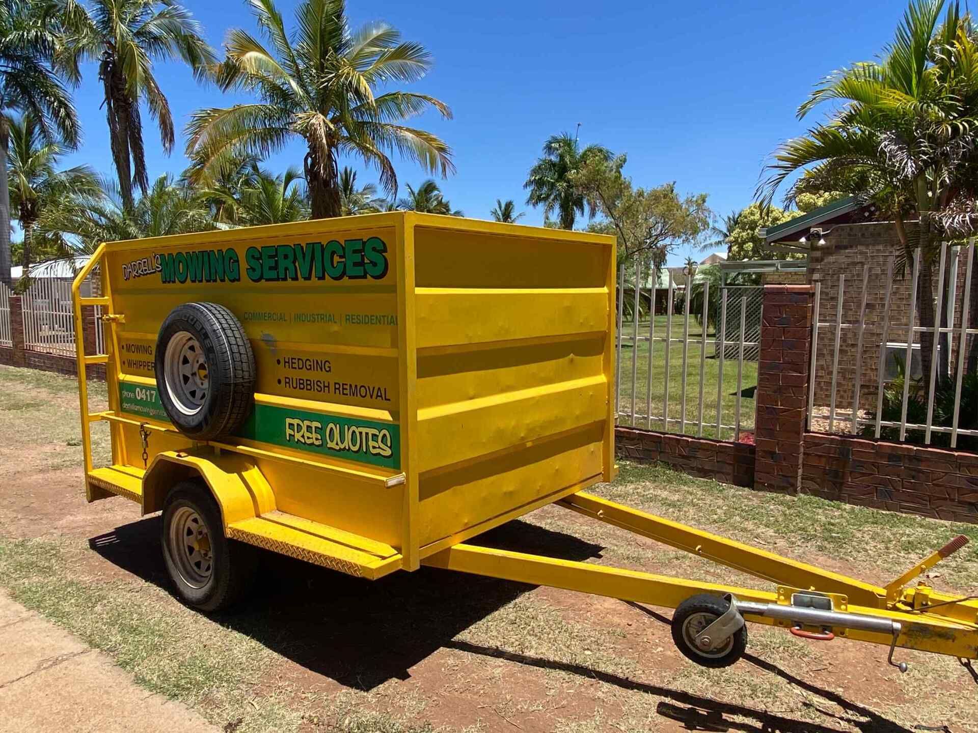 Yellow Utility Trailer With Company Signage Parked Outdoors — Darrell's Mowing Services in Sunset, QLD