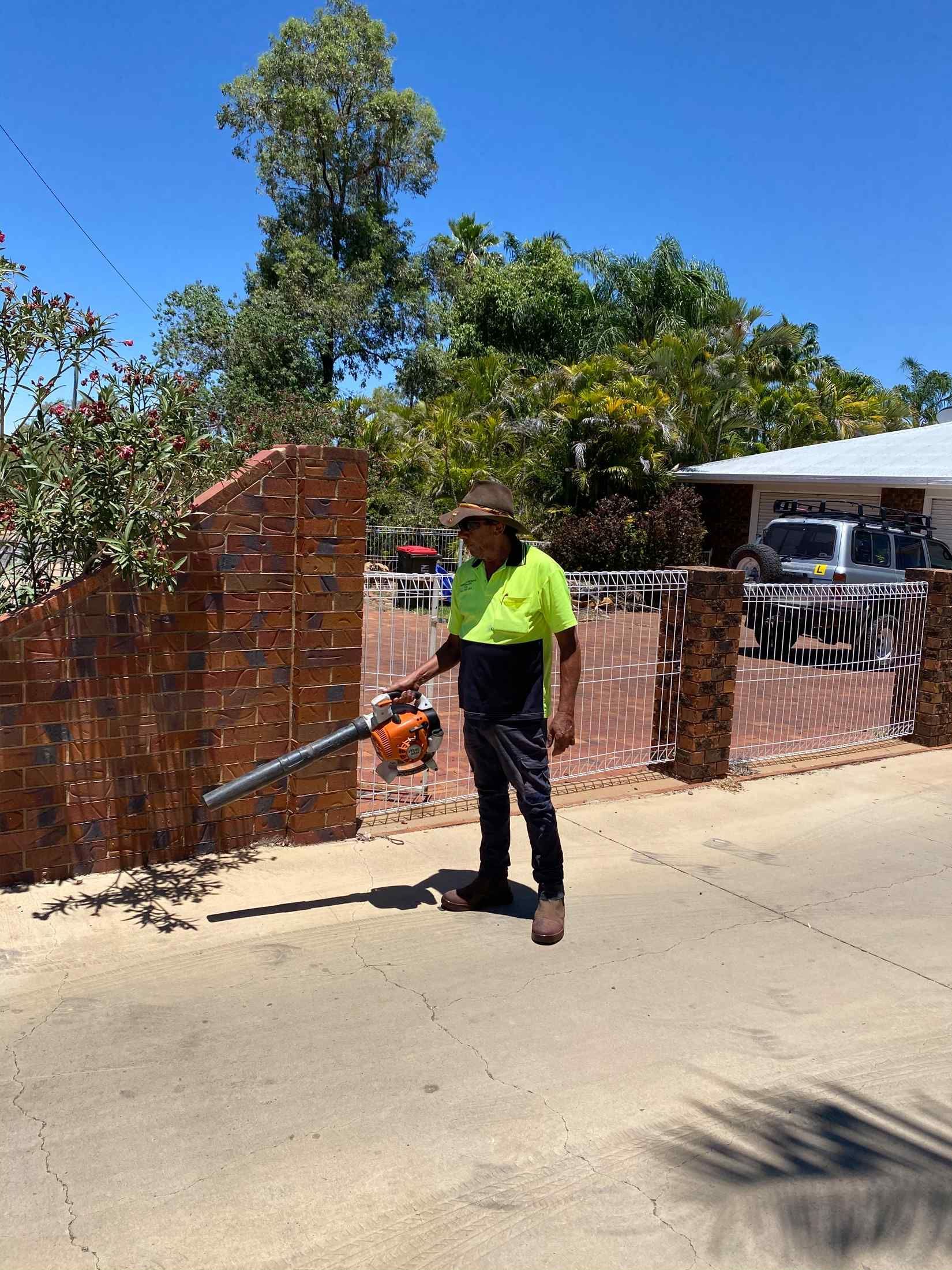 Person in Neon Green Shirt Uses a Leaf Blower to Clear a Brick Driveway — Darrell's Mowing Services in Sunset, QLD