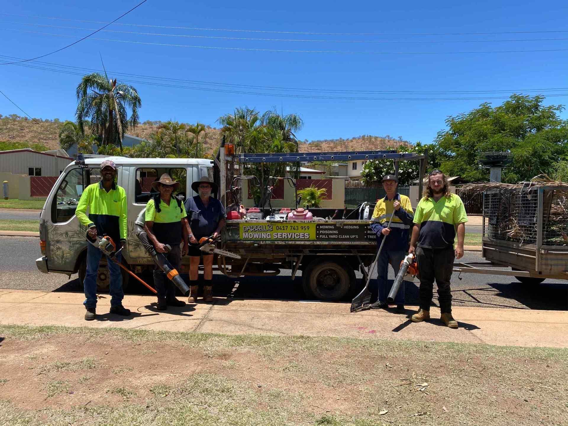 Five People in Safety Vests Stand with Yard Tools by A Truck in A Sunny Street — Darrell's Mowing Services in Cloncurry, QLD
