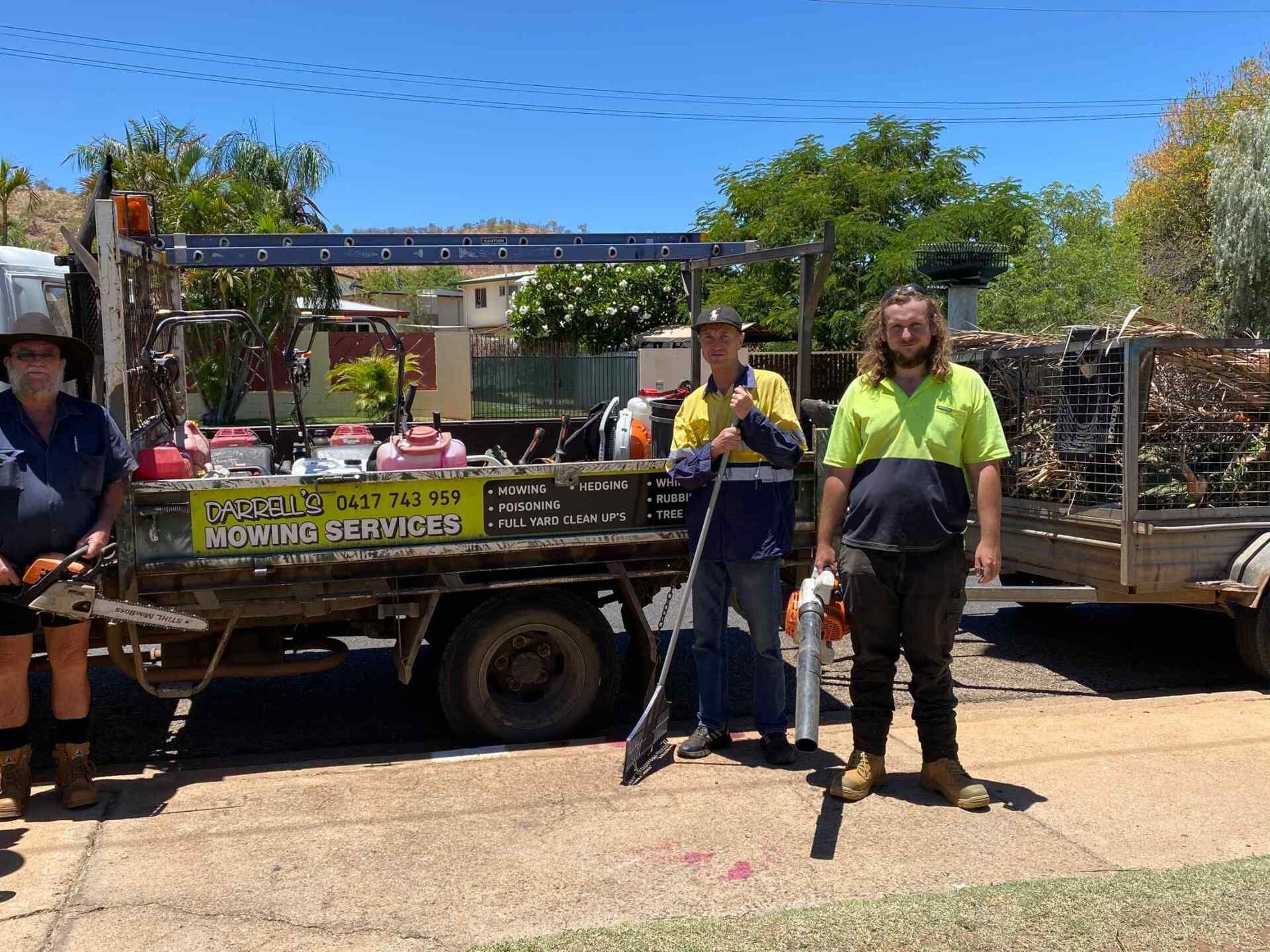 Three People With Gardening Tools Stand Near a Truck and Trailer Outdoors — Darrell's Mowing Services in Sunset, QLD