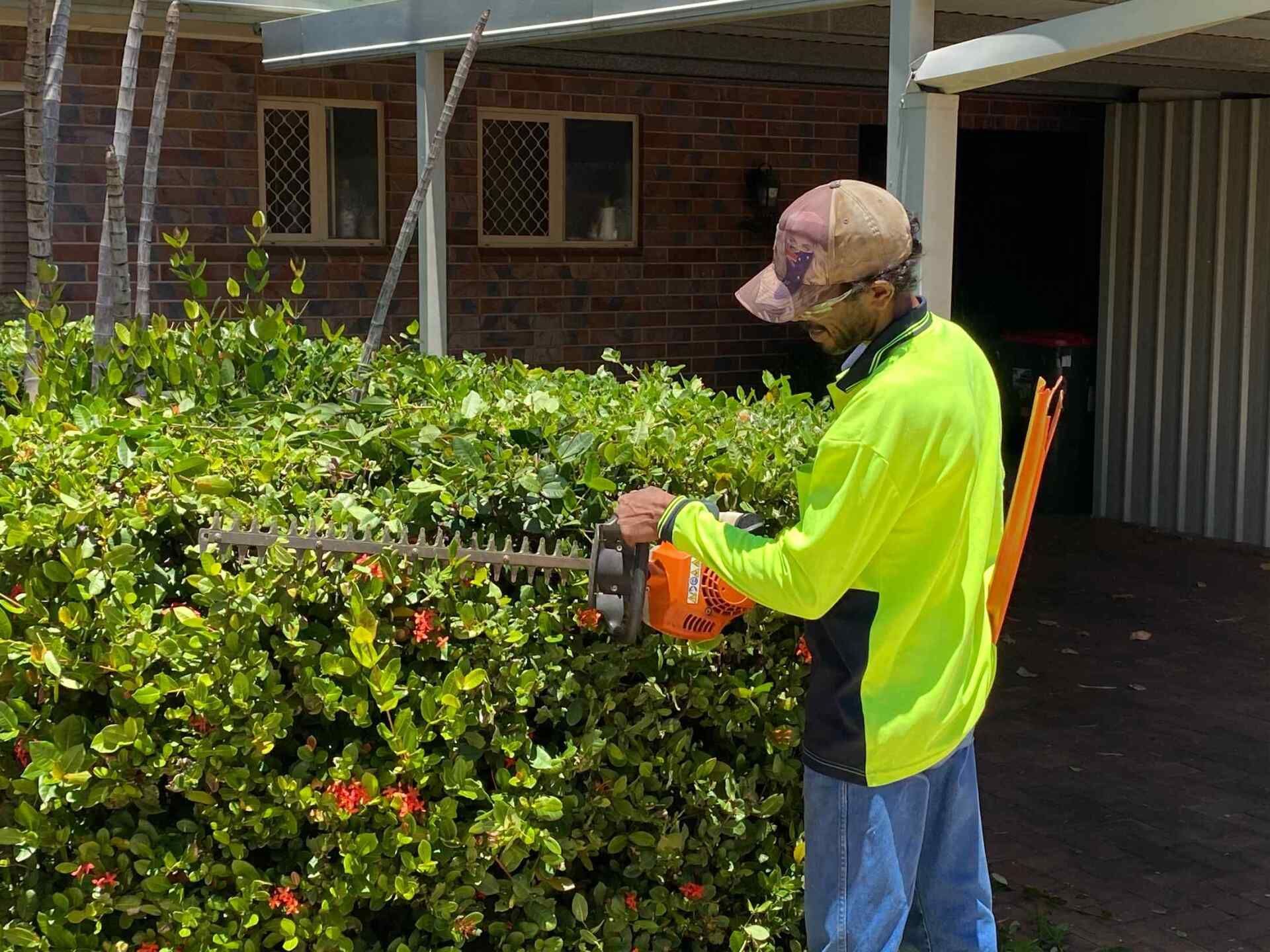 Man in Neon Shirt Trims a Green Hedge With a Power Trimmer — Darrell's Mowing Services in Sunset, QLD