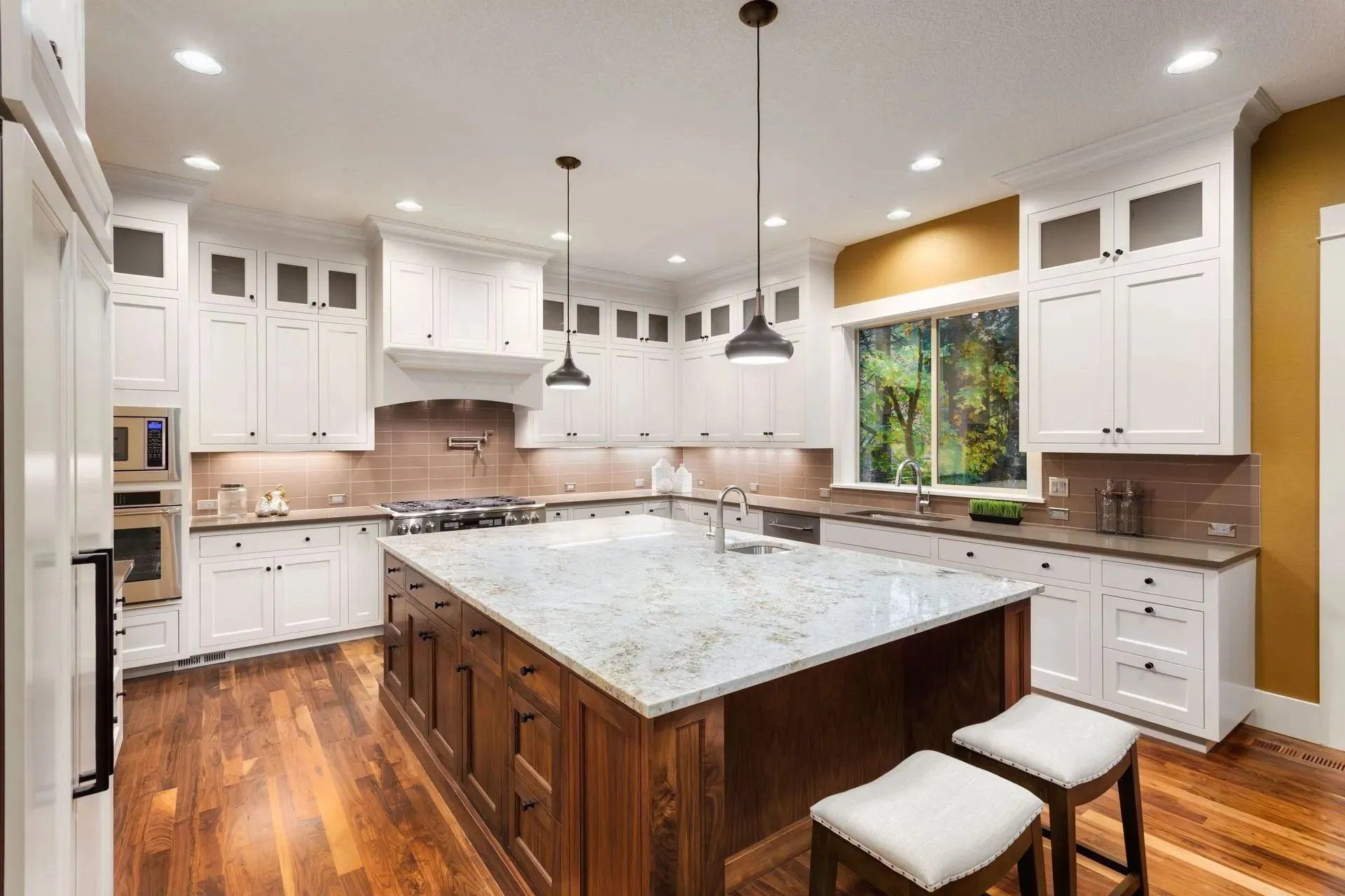 Bright modern kitchen with white cabinets, marble island, wood floors, and pendant lights